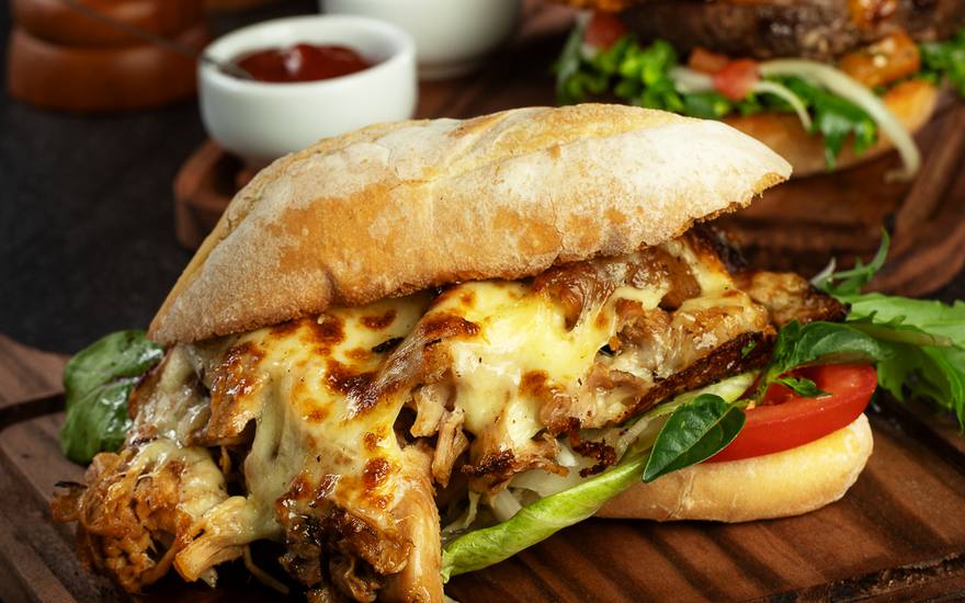 Sanduíche de carne desfiada com queijo gratinado em pão rústico, servido na tábua